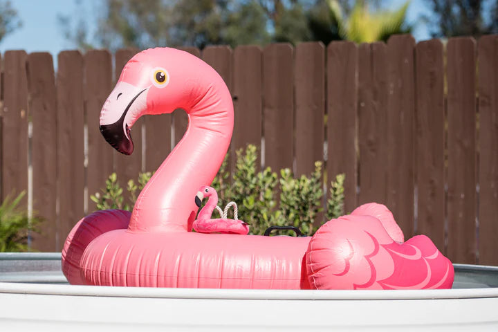 Inflatable pink flamingo pool float on a pool with a wooden fence and plants in the background